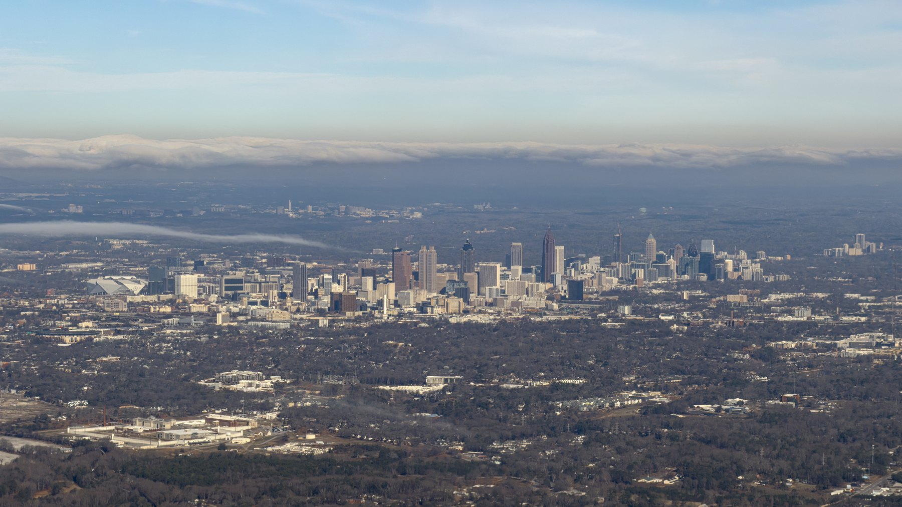 Daytime aerial of Downtown Atlanta skyline (Bank of America Plaza spire, 191 Peachtree, Georgia-Pacific Tower) with Mercedes-Benz Stadium’s distinctive fan-shap