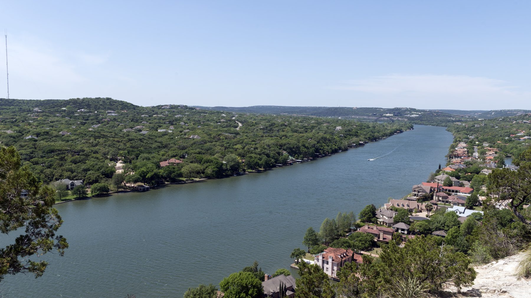 View of Lake Austin from Mount Bonnell (Covert Park), Hill Country ridgeline and lakeside rooflines below, clear blue midday light -- brief VISUAL IDENTITY #4 s