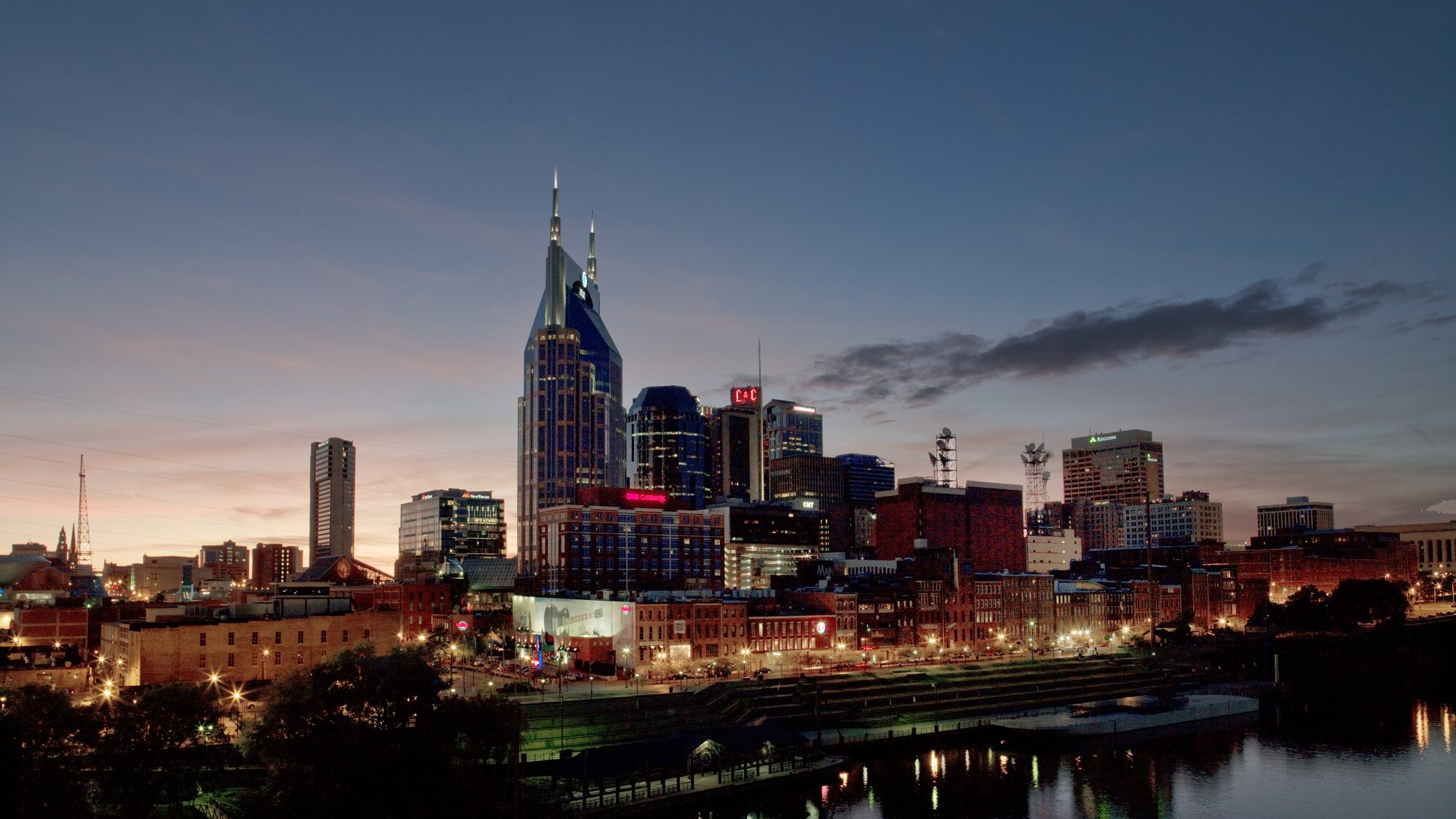 The Batman Building (AT&T Building, 333 Commerce St) over the Cumberland River at blue hour, twin spires against a dusk gradient sky, reflections in the water