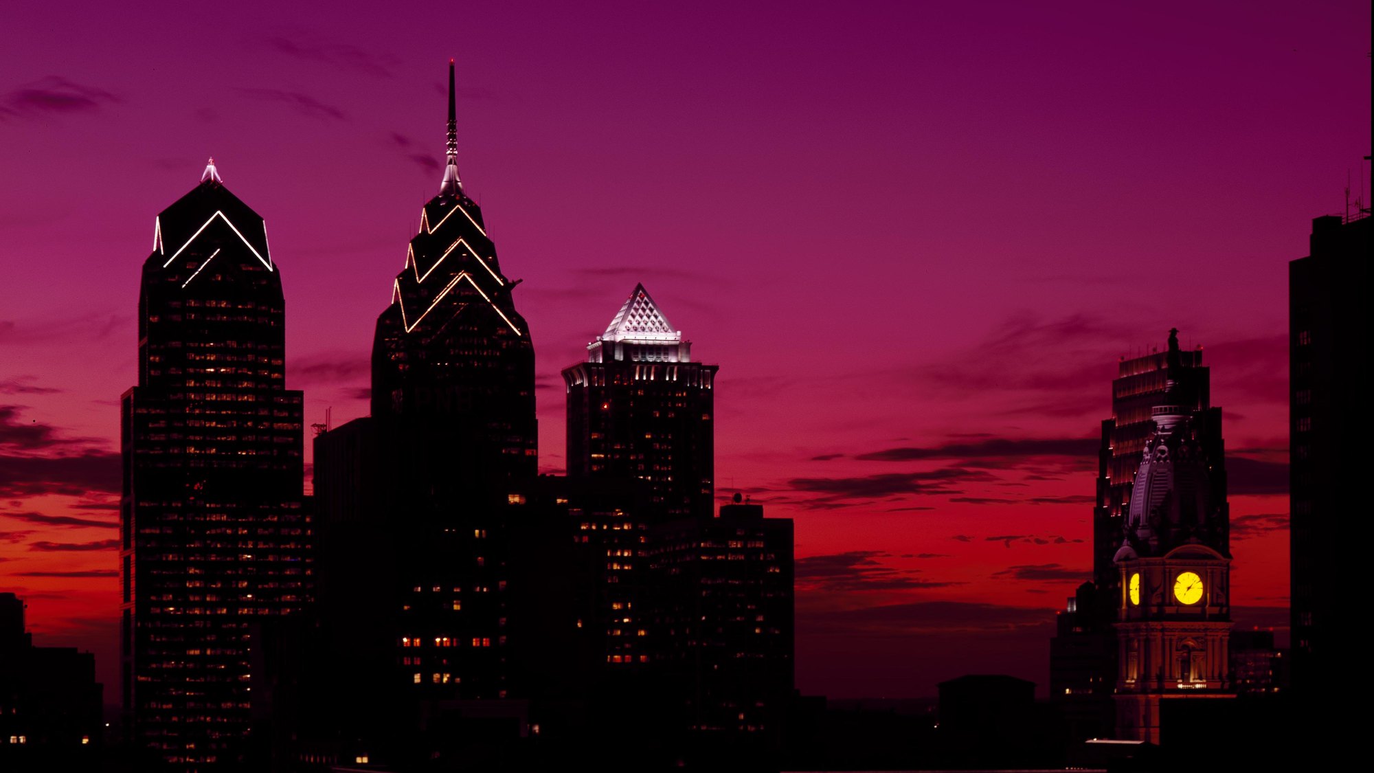 Downtown Philadelphia skyline in deep sunset silhouette -- Liberty Place towers + City Hall/Billy Penn clock tower, saturated magenta-orange sky