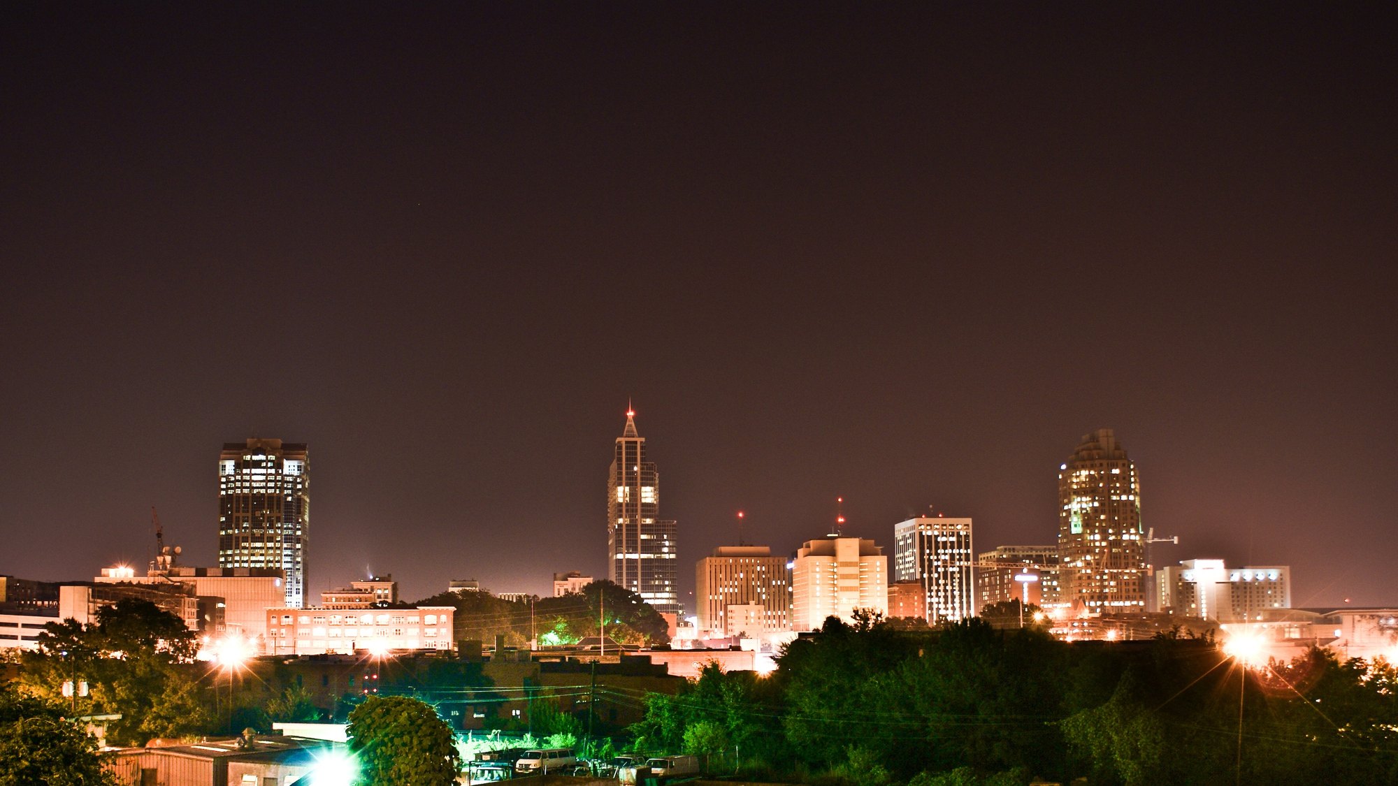 Downtown Raleigh skyline at night from Boylan Ave -- PNC Plaza’s illuminated crown spire dead-center with red beacon, Wells Fargo Capitol Center’s stepped crown
