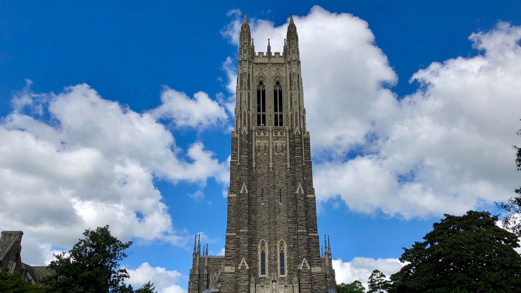 Duke Chapel’s 210-ft Gothic bell tower, West Campus, Duke University, Durham -- full height from base entrance to twin corner pinnacles, clear blue sky with cum