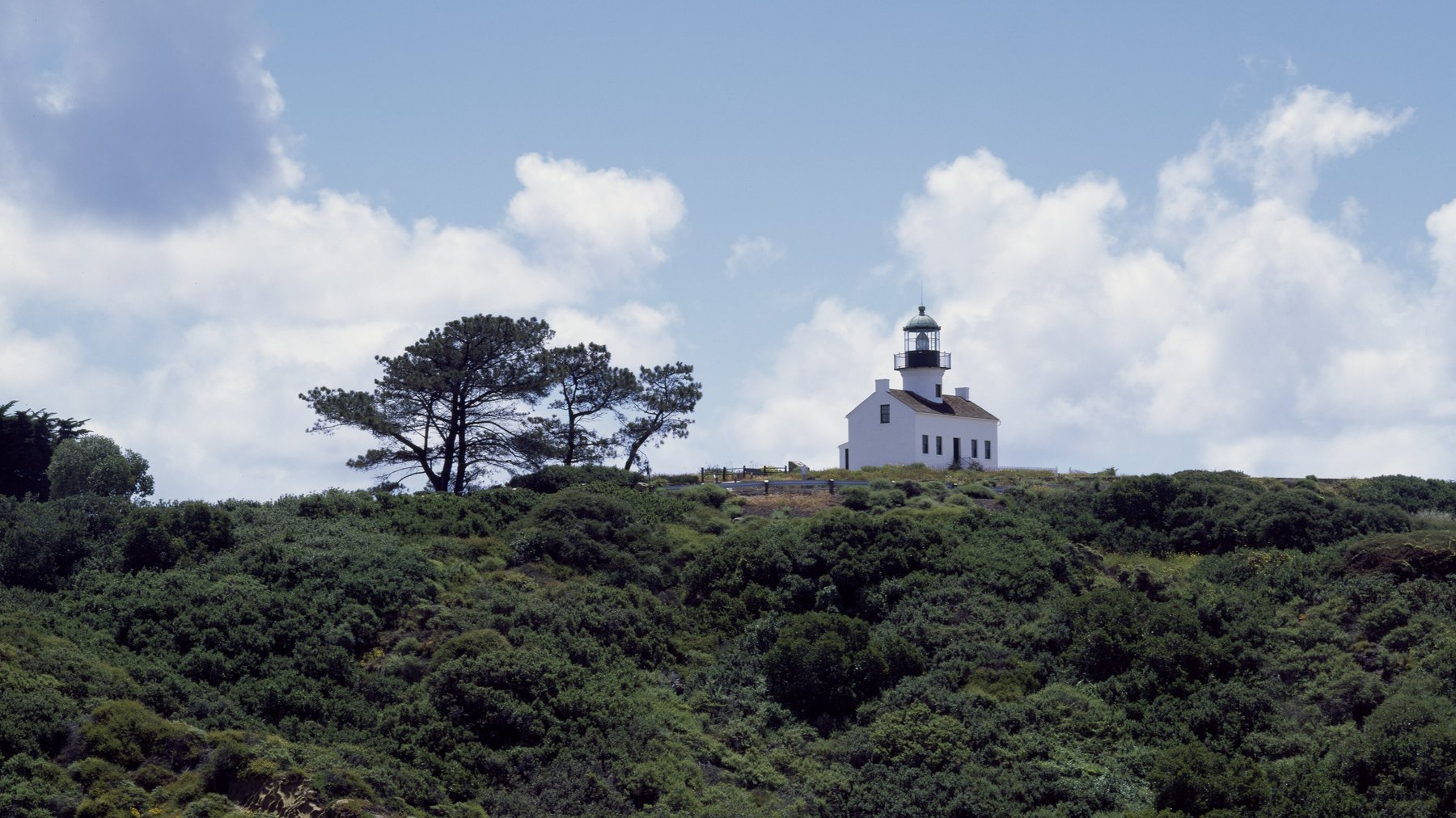 Old Point Loma Lighthouse (1855) at Cabrillo National Monument, white keeper’s cottage + black lantern room on the Point Loma bluffs, clear daylight -- SD’s #3