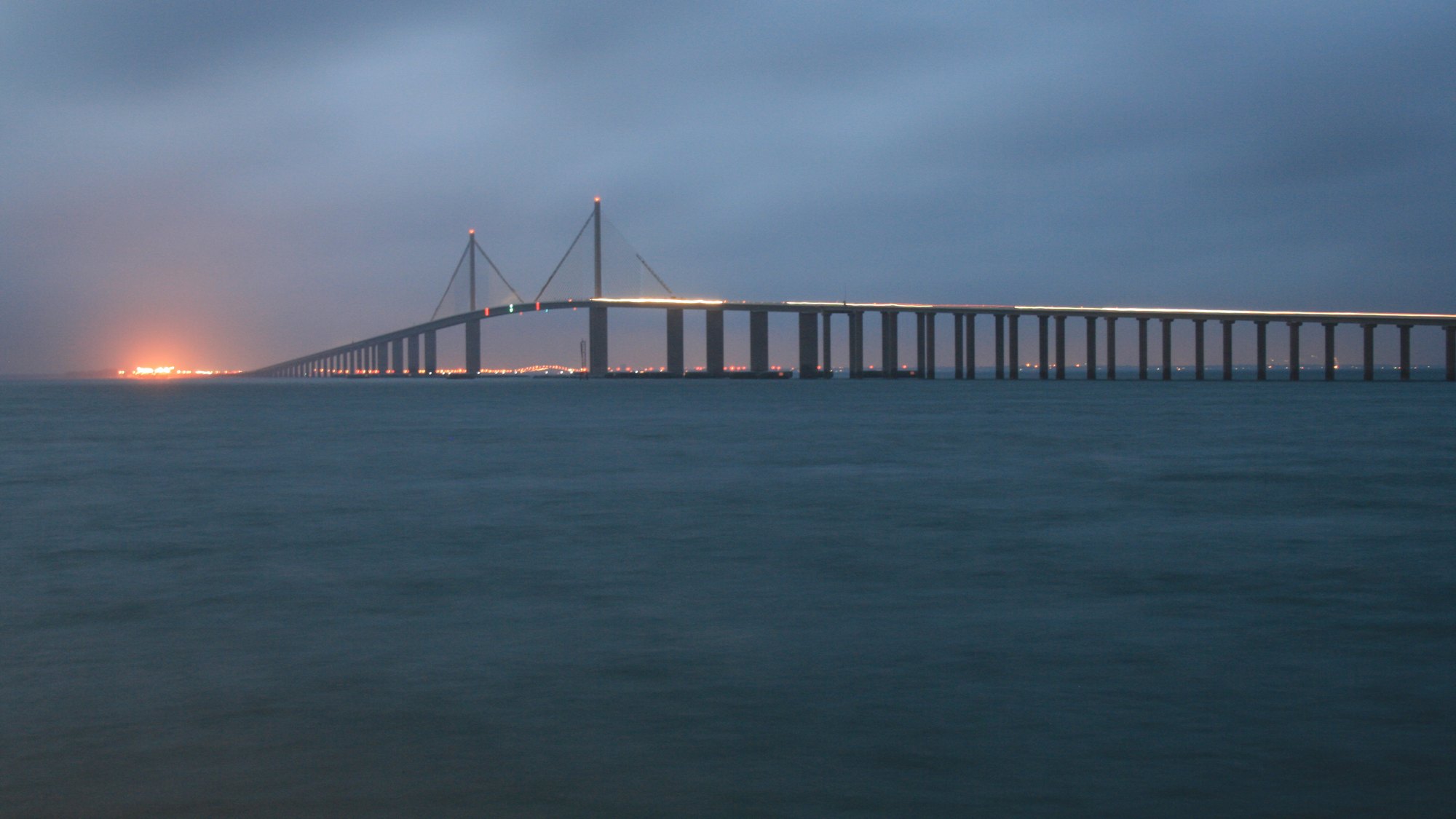 Sunshine Skyway Bridge at dusk, viewed from the pier -- the gold-lit cable towers over Tampa Bay, brief VISUAL IDENTITY #1 subject, THE image residents claim